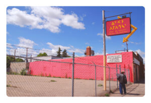 A pink low-rise commercial building with a pink sign in Cree syallabics against a blue sky