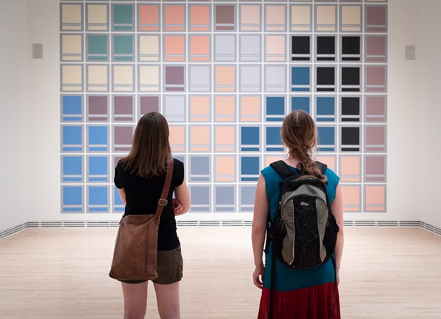 Two people look at a wall painted in a colourful grid in an art gallery.