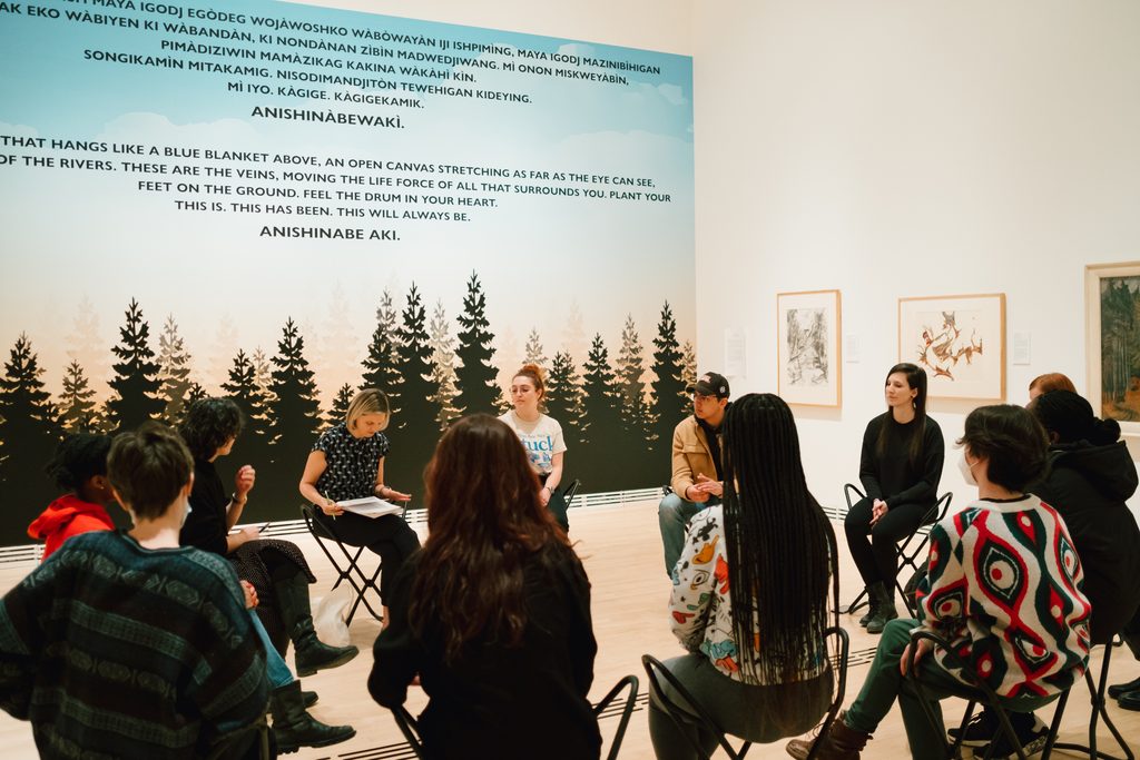 A group of students seated in a circle for an exhibition tour