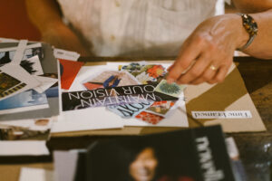 A hand arranges cut-out magazine pictures into a collage arrangement.